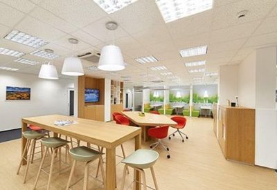 Spacious communal breakout area with light wood tables, red chairs, and modern pendant lighting.