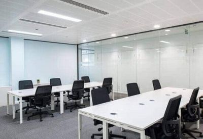 Modern open-plan office with white desks, black ergonomic chairs, and a glass partition wall.