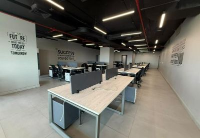 Open-plan office area with rows of modern white desks and black ergonomic chairs.