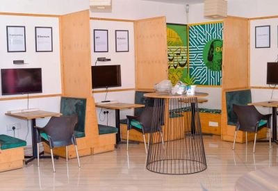 Coworking area featuring semi-private wooden booths with monitors and teal cushioned seating.