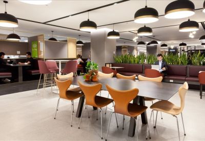 Vibrant communal lounge featuring designer chairs, rows of pendant lights, and indoor greenery.