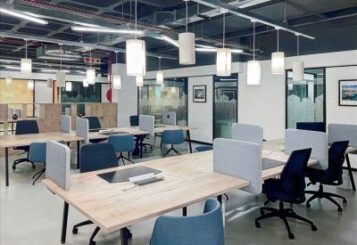 Modern open-plan office with light wood desks and blue ergonomic chairs.