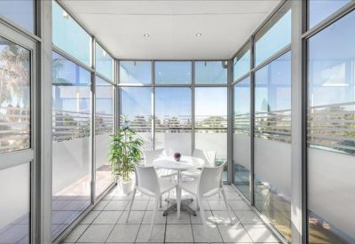 Glass-walled sunroom balcony with a small table and chairs overlooking the city.