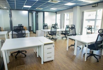 Bright open-plan office with white desks and black mesh ergonomic chairs.
