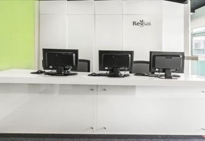 Minimalist white reception desk with branded backdrop and computer monitors.
