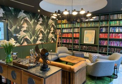 Vibrant communal lounge with a floor-to-ceiling rainbow bookshelf and tropical leaf wallpaper.