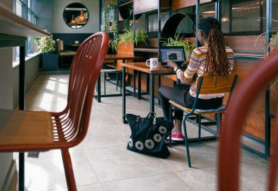 Bright coworking space featuring wooden desks, indoor plants, and a person working on a laptop.