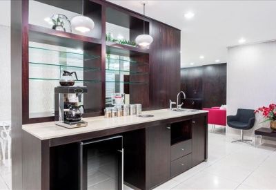 Modern communal kitchen and coffee station with dark wood cabinetry and glass shelving.