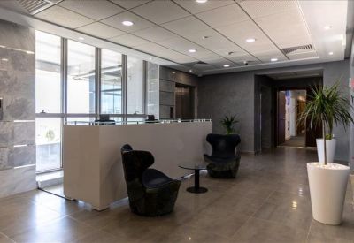 Modern reception lobby with a sleek white desk, black lounge chairs, and potted plants.