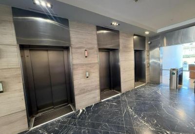 Elevator bank with three stainless steel doors and polished dark marble flooring.