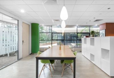 Modern communal area with long wooden table, green chairs, and unique drop lighting.