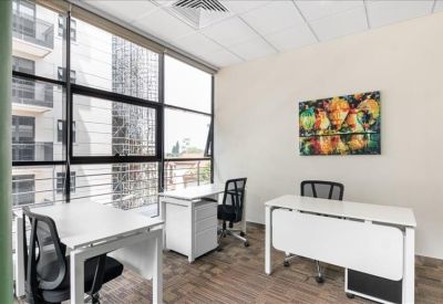 Bright private office with three white desks and floor-to-ceiling windows.