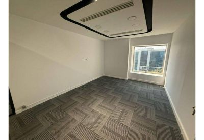 Empty corner office with natural light from a large window and patterned carpet.