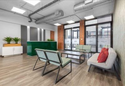 Modern reception area with a green glass desk, grey accent wall, and lounge seating.
