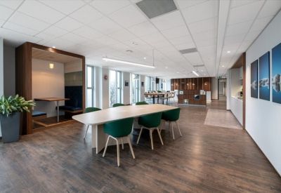 Modern communal area with wooden floors, a long dining table with green chairs, and a private wooden booth.