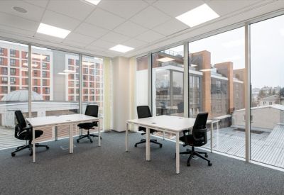 Minimalist office space with white desks and black chairs positioned near floor-to-ceiling windows.