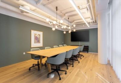 Sleek meeting room featuring a long wooden table, grey chairs, and a large wall-mounted screen.