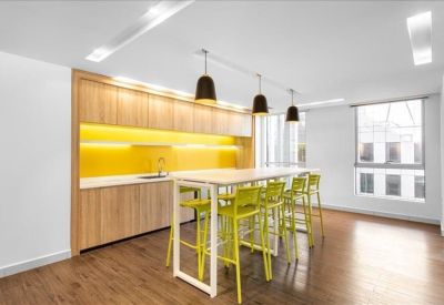 Modern communal kitchen area with wood-finish cabinets, yellow backsplash, and high-top seating.