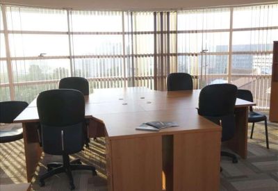 Light wood coworking desk with black chairs and large windows.