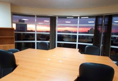 Large boardroom table with black chairs and a panoramic sunset view through the windows.