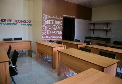Spacious communal coworking area with multiple desks and a kitchen counter in the background.