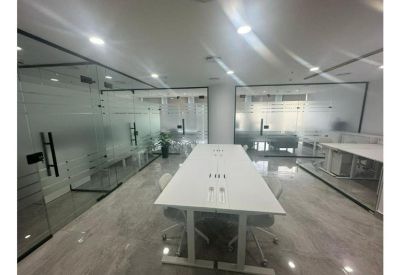 Bright, open-plan communal workspace with long white tables and glass partitions.