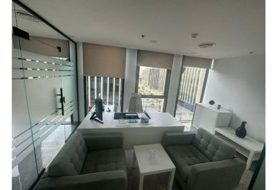 Private office suite with a large desk, grey armchairs, and city views through large windows.