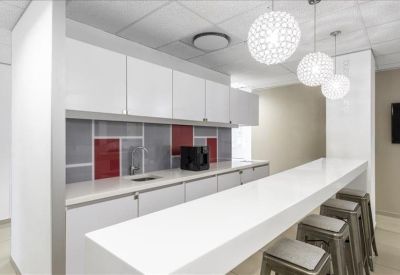 Modern break area with a white breakfast bar, bar stools, and red accent backsplash.