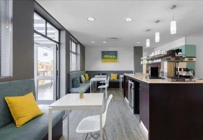 Modern breakout area with a coffee bar, booth seating, and yellow cushions.
