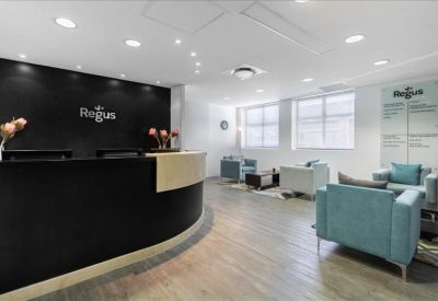 Wide-angle view of a bright reception lobby with teal armchairs and a black desk.