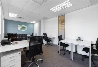 Bright workspace featuring several white desks and ergonomic black chairs.