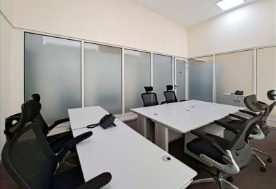Meeting room with two long white desks and black ergonomic chairs against frosted glass partitions.