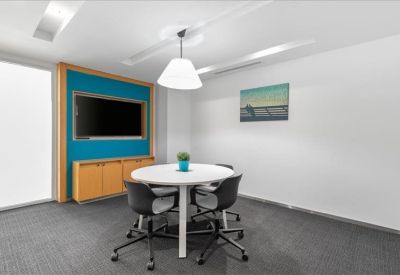 Small meeting room with a round white table, teal accent wall, and flat-screen TV.
