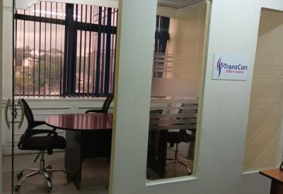 Open-plan workspace with multiple wooden desks and black ergonomic chairs near a large window.
