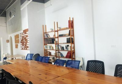 Long communal wooden table with blue mesh chairs and a tall bookshelf.