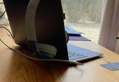 A laptop and headphones on a wooden desk with a sunny sky and palm trees outside.