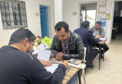 Three men sitting at small wooden tables, focused on paperwork and discussion.