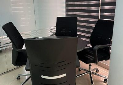 Small round meeting table with four black mesh office chairs and striped window blinds.