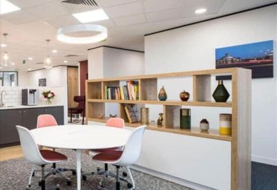 Vibrant communal breakout area with a round table, pink chairs, and a decorative bookshelf.