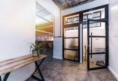 Office entrance with a glass door, industrial black frames, and a wooden console table with a plant.