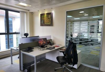 Bright corner workstation with a white desk, ergonomic chair, and glass partition.