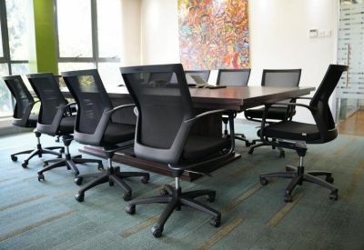Spacious boardroom with a long wooden table, black mesh chairs, and abstract wall art.