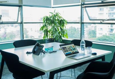 Bright private office suite with a white desk, laptop, and large windows overlooking the city.