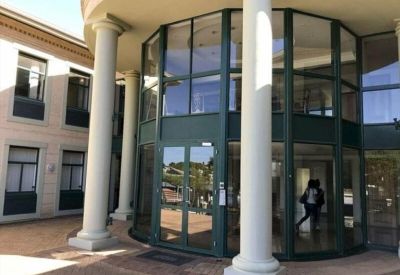 Curved glass building entrance with white pillars and double doors.