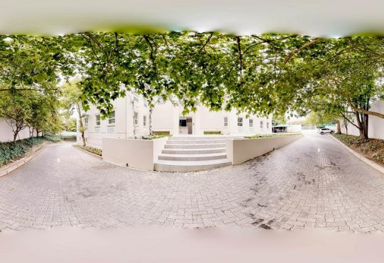 Wide-angle exterior view of the building and driveway framed by lush green trees.