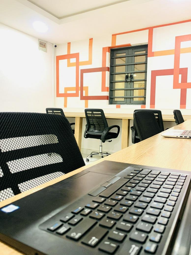 Open-plan coworking space at 1 Ogunnusi Road with wooden desks and a geometric orange wall mural.