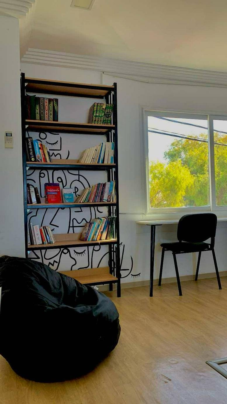 Lounge area at 12 Rue de la Municipalité featuring a black beanbag, wooden bookshelf, and illustrated wall.