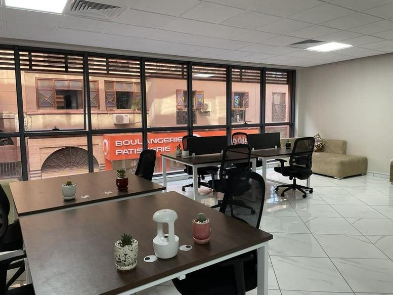 Open office area featuring multiple wooden desks, ergonomic chairs, and city view windows.