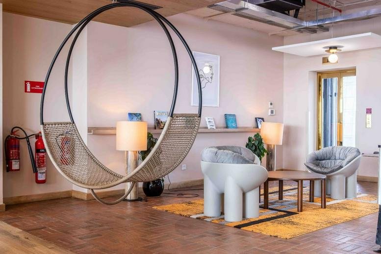 Unique lounge featuring a large circular hanging chair, modern white armchairs, and warm lighting.