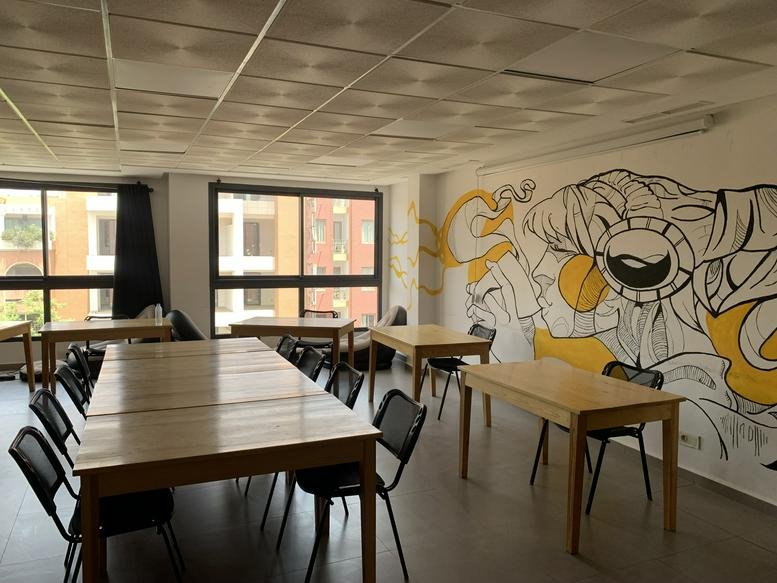 Spacious coworking area with wooden tables and a vibrant graphic wall mural at Rendezvous Dar, Boulevard Moulay Rachid.